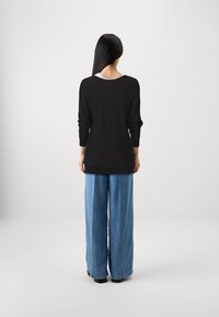 Maglione nero a maniche lunghe in maglia con scollo a barca, abbinato a pantaloni in denim azzurro chiaro a gamba larga. Tessuto morbido, vestibilità rilassata.