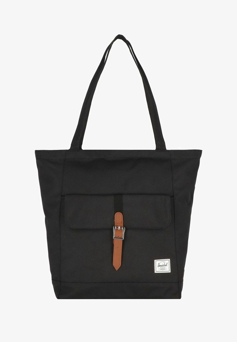 Sac cabas noir avec des longues poignées, poche avant sécurisée par une sangle à boucle marron et une étiquette de marque blanche en bas à droite.