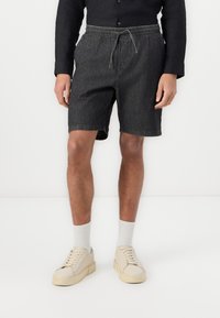 Shorts en denim noir avec une taille élastique et un cordon de serrage. À associer avec des baskets beiges et des chaussettes blanches. Design simple, coupe à mi-genou.
