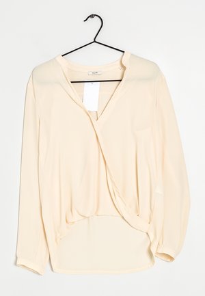 Blouse rose clair avec un col en V, des manches longues et un design enroulé. Fabriquée dans un tissu lisse avec une coupe ample et un ourlet incurvé.