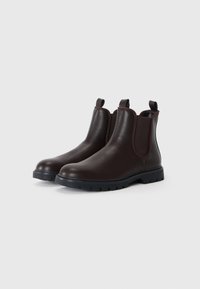 Botas de piel marrón hasta el tobillo con paneles laterales elásticos, acabado texturizado, puntera redonda y lengüetas de tiro, que cuentan con una suela de goma negra resistente.