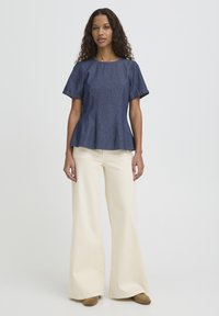 Haut en jean style péplum avec manches courtes, col rond et couleur bleu clair. Associé à un pantalon ample crème et des chaussures marron.