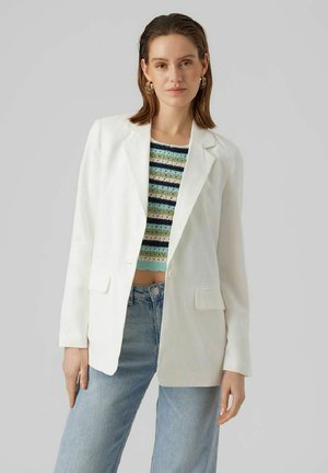 Blazer blanc avec revers crantés, deux poches avant et une coupe décontractée, porté sur un crop top rayé multicolore et un jean bleu clair.