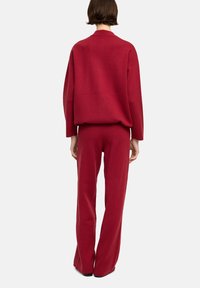 Czerwony zestaw dzianinowy z luźnym swetrem i wysokim dekoltem oraz pasującymi spodniami z szerokimi nogawkami. Gładka tekstura; prosty, spójny design.