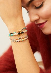 Trois bracelets empilés présentant des designs tressés et perles dans des tons turquoise, noir et accents dorés, exposés sur un poignet contre un fond doux.