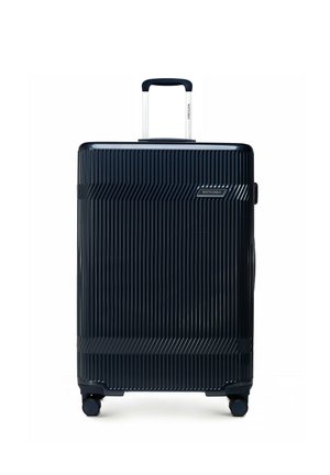 Granatowa, twarda walizka z pionowymi rowkami, teleskopową rączką, czterema kółkami oraz oznaczeniem marki „Wittchen” na przedniej części i uchwycie.