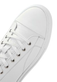Baskets blanches avec une tige en cuir lisse, un bout arrondi et une semelle en caoutchouc blanc contrastant. Équipées d'œillets métalliques et de lacets plats.
