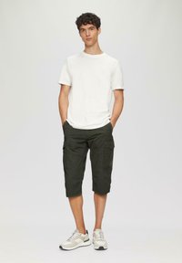 Weißes Rundhals-T-Shirt, olivgrüne Cargo-Shorts mit Seitentaschen und graue Sneakers mit schwarzen Akzenten, die vor einem hellen Hintergrund stehen.