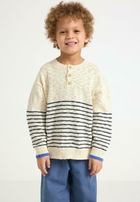 Lys beige strikket sweater med marineblå vandrette striber og tre træknapper ved halsen. Har ribbede manchetter med blå accenter.