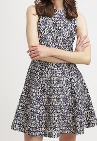 Navy- und cremefarbenes Spitzekleid mit engerem Oberteil und ausgestelltem Rock. Es besitzt ein ärmelloses Design und ein aufwendiges Blumenmuster.