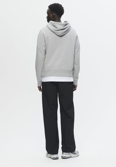 Grauer Kapuzenpullover mit Kapuze, gerippten Bündchen und Saum, kombiniert mit lockeren schwarzen Hosen und silbernen Sportschuhen.
