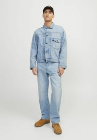 Veste en jean bleu clair avec poches avant, associée à un jean droit bleu clair. Des bottes marron complètent la tenue.
