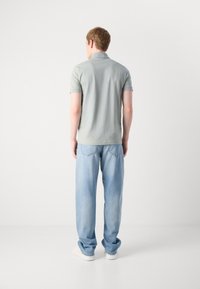 Lys grønn polo skjorte med kort krage, kombinert med lyseblå avslappede jeans; bomullsmateriale, glatt tekstur og enkle søm detaljer.