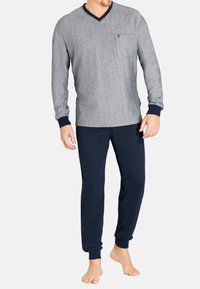 Graues Langarmoberteil mit einem marineblauen V-Ausschnitt und einer Brusttasche, kombiniert mit marineblauen Jogginghosen. Der Stoff wirkt weich und bequem.