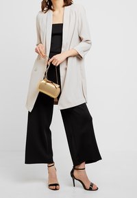 Ljust grå kavaj med uppvikta ärmar, kombinerad med svarta vida byxor och en svart strapless-topp. Håller en clutchväska i guldmetall.