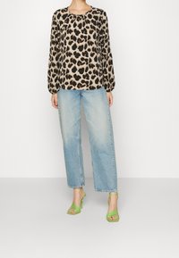 Leopardenmuster-Bluse mit langen, puffigen Ärmeln, kombiniert mit hochgeschnittenen, hellblauen, geraden Jeans und grünen, r strapped Heels.