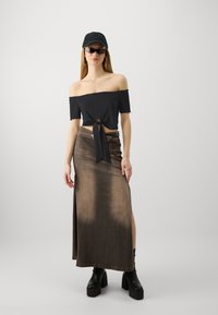 Must värviline off-shoulder crop top, millel on ees seotud detail, on kombineeritud pika pruunist denimist seeliku ja platvormikingadega, millel on külgmised lõhikud.