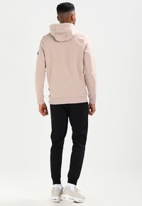 Felpa con cappuccio rosa chiaro, maniche a costine e fondo a costine, abbinata a pantaloni jogging neri. Dettagli notevoli includono una consistenza morbida e una grafica minima.