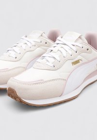 Un par de zapatillas Puma blancas y beige con cordones blancos, logo de Puma dorado, detalles en rosa y suelas marrones con relieve.