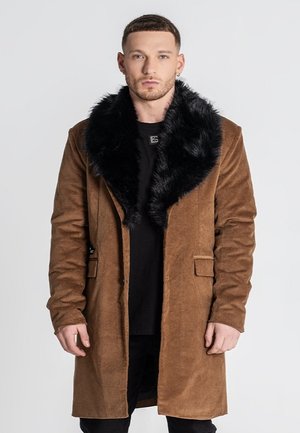 Cappotto in suede marrone con colletto in pelliccia sintetica nera, maniche lunghe, chiusura con bottoni e due tasche frontali, caratterizzato da una finitura testurizzata.