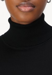 Svart genser med høy hals og ribbestruktur, har en tettsittende design som fremhever et glatt og mykt stoff.