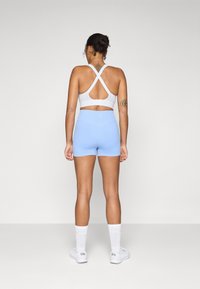 Soutien-gorge de sport blanc avec bretelles croisées, associé à un short bleu clair. Le matériau est extensible ; il présente une taille mi-haute et une texture lisse.