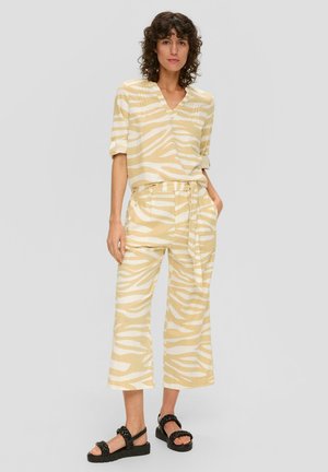 Blusa a righe gialle e bianche con scollo a V e maniche arrotolate, abbinata a pantaloni larghi coordinati. Sandali con piattaforma neri completano il look.