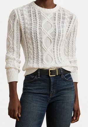 Personne portant un pull en maille torsadée crème rentré dans un jean bleu foncé avec une ceinture noire avec une boucle dorée.