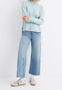 Light blue knit sweater with a crew neckline and side slits, paired with light-wash wide-leg jeans and white sneakers with black accents.