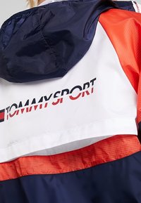 Kurtka w kolorach granatowym, białym i czerwonym z blokowaniem kolorów, z logo Tommy Sport na plecach i przypiętym granatowym kapturem.