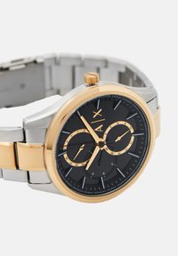 Kovinska ura s črnim številčnikom, z zlatimi detajli in dvema podštevilčema. Ima srebrno-zlati dvojnobarvni pas in ozko obrobo.