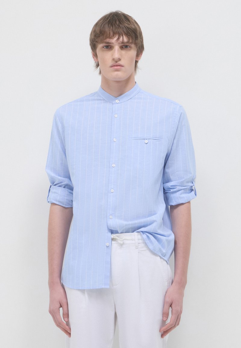 Camicia a maniche lunghe blu chiaro con sottili righe bianche verticali, colletto con bottoni, taschino sul petto, maniche arrotolate e tessuto liscio.