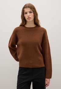 Maglione marrone lavorato a maglia con scollatura rotonda, bordo e polsini a costine. Tessuto morbido e vestibilità rilassata, indossato con pantaloni neri aderenti.