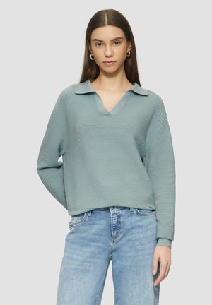 Light blue ribbed sweater with a V-neck and collar, featuring long sleeves and a relaxed fit, paired with light blue denim jeans.