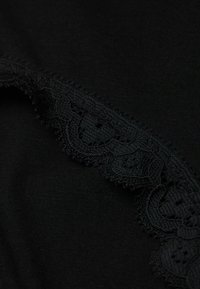 Svart tyg med en strukturera spetskant som har utsökta mönster längs en kant. Spetsen uppvisar intrikata detaljer och en scallop-design.