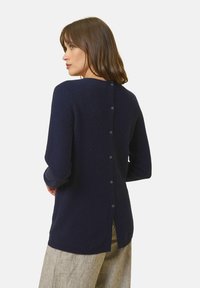 Maglione blu navy con scollatura rotonda, maniche lunghe e chiusura con bottoni sul retro. La texture morbida e le aperture laterali aumentano il comfort.