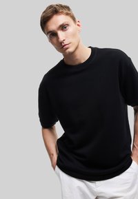 Zwart crewneck t-shirt met een relaxte fit, voorzien van korte mouwen en een zachte textuur, gecombineerd met witte lichtgewicht broek.