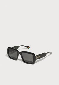 Occhiali da sole neri a forma rettangolare con lenti grigie, montatura in plastica spessa e logo Polaroid dorato sulla tempia. Dettaglio arcobaleno sulla punta dell'asta.