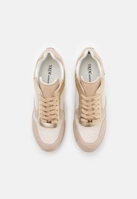 Tan and gold sneakers with a textured finish, featuring a padded collar, metallic accents, and flat laces. Reinforced rubber sole.