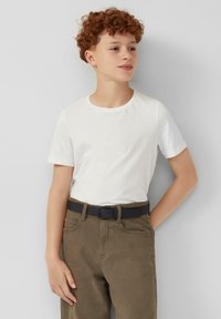 Witte T-shirt met korte mouwen, gecombineerd met olijfgroene broeken, met een zwarte riem. De stof lijkt glad en heeft een getailleerde pasvorm.