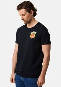 Sort bomulds t-shirt med et farverigt grafisk motiv af peberfrugter og tekst på brystet. Korte ærmer og rund halsudskæring. Casual pasform.