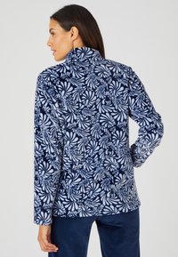 Maglione in pile navy con motivo floreale bianco, colletto alto e maniche lunghe. Tessuto morbido con design uniforme e vestibilità comoda.