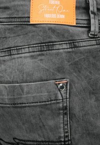 Grå denimjeans med en orange etikett som säger "Forever Street One Fabulous Denim." Inkluderar en liten ficka med detaljer i silverknapp.