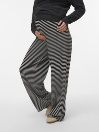 Μαύρο-άσπρο ριγέ παντελόνι εγκυμοσύνης με φαρδιά μπάρα από μαλακό, υφασμάτινο ύφασμα με υφή. Συνδυασμένο με σκούρο πουλόβερ και ουδέτερα παπούτσια.