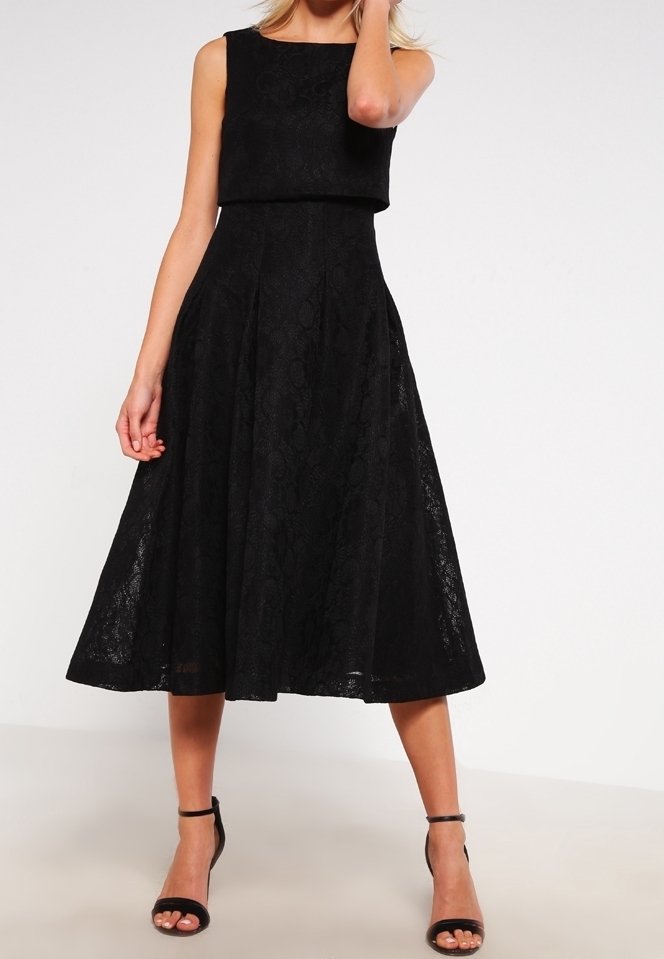 Robe midi noire en dentelle sans manches avec taille cintrée et jupe évasée, portée avec des sandales à talons hauts noires à bride cheville.