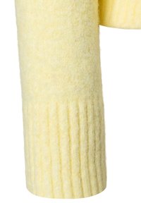 Gelber gestrickter Pulloverärmel mit weicher, flauschiger Textur und einem gerippten Bündchen. Der Stoff wirkt leicht und gemütlich.