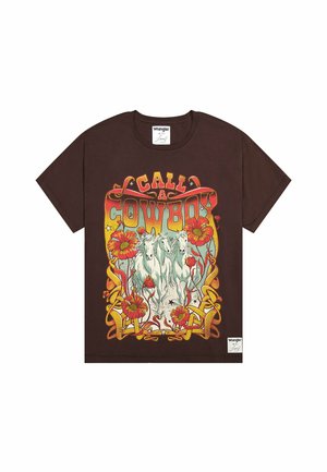 T-shirt en coton marron avec un design graphique présentant deux chevaux blancs, des fleurs rouges et le texte "APPELE UN COWBOY" dans une police décorative.