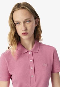 Polo shirt rosa realizzato in un tessuto testurizzato, con colletto, patta con tre bottoni e un piccolo logo ricamato sul petto.