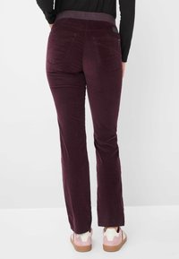 Bordeauxfarbene Cordhosen mit einem taillierten Bund, zwei Gesäßtaschen und einer weichen Textur. Leichter Schlag am Saum, kombiniert mit rosa Schuhen.