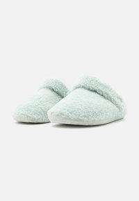 Ett par ljusblå mjuka fleeceinomhusskor med rundad front och vikbar manschett, visade mot vit bakgrund.